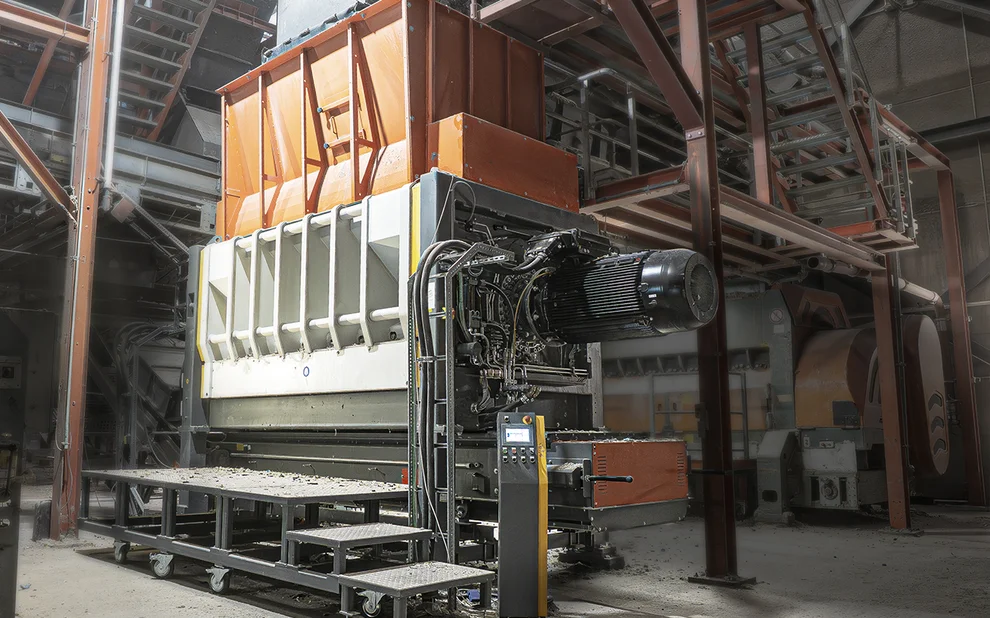Industrielle Brecheranlage mit großem Motor und orangefarbenem Aufgabetrichter in einer Fabrikhalle